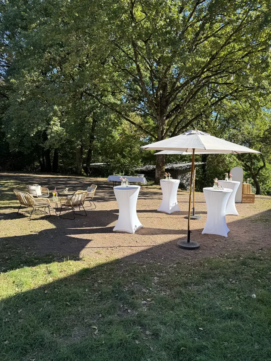 Outdoor drinks reception at Forsthaus Neuhaus with white standing tables and parasols beneath the trees